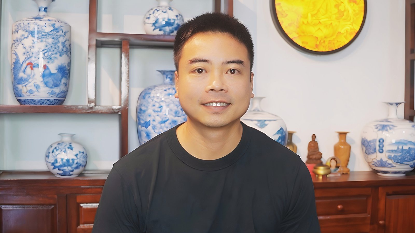 Nguyen Duy Phong, who teaches the video lessons, smiling in front of a shelf of blue-and-white vases