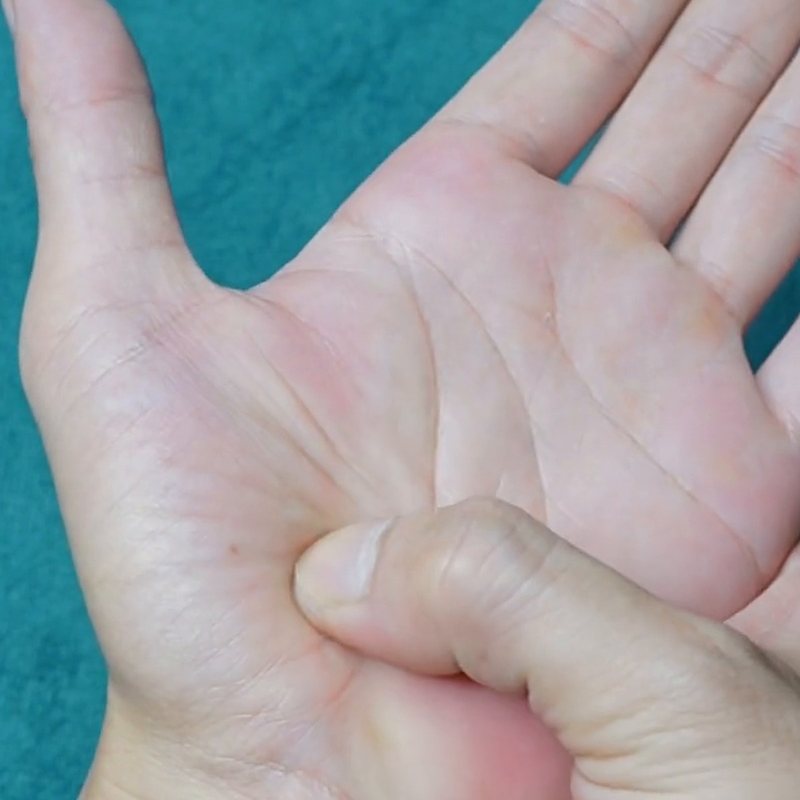 A thumb pressing the fleshy pad at the base of the thumb, on an open palm