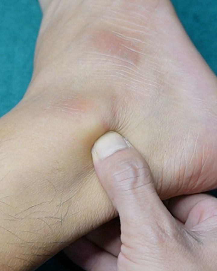A thumb pressing the hollow behind the outer ankle bone, next to the heel